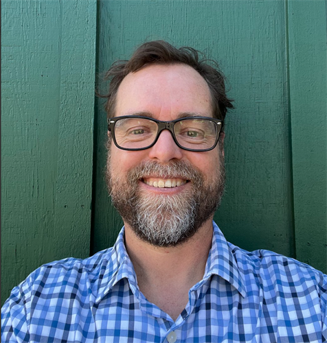 smiling white man with brown hair, a beard, and glasses